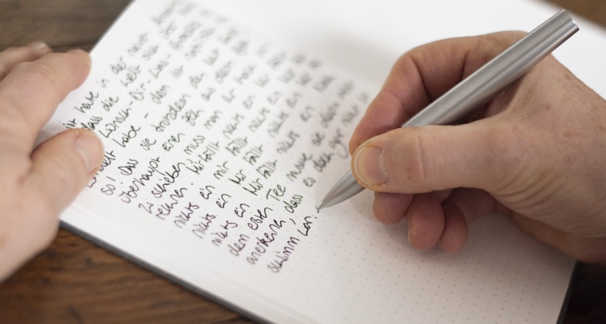 Hand schreibt mit Rollerball oder Tintenroller einen Text in ein Notizbuch von Hahnemühle.