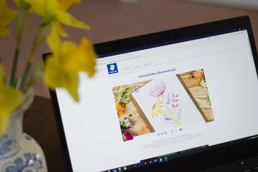 Auf einem aufgeklappten Laptop sieht man die Anleitung zum Malen einen Blumenstraußes aus der Design Journey von Staedtler.