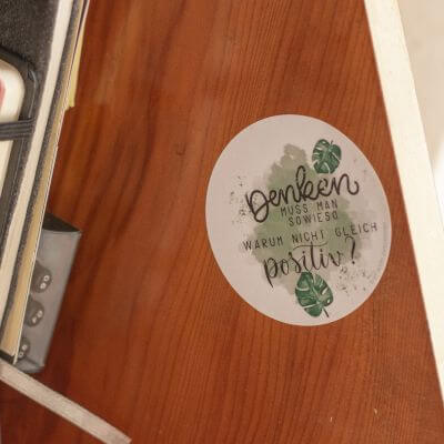Ein runder Aufkleber von Avery Zweckform klebt auf Holz. Auf ihm steht in Handlettering: "Denken muss man sowieso, warum nicht gleich positiv?"