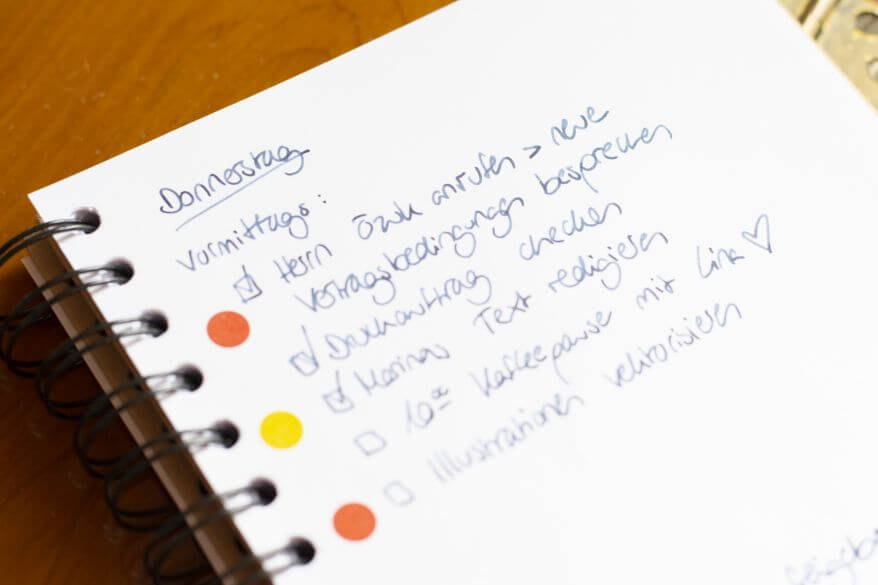 Nahaufnahme eines aufgeschlagenen Notizbuchs mit Tagesplan für den Donnerstag. Einzelne Stellen sind mit Markierungspunkten von Avery Zweckform markiert.
