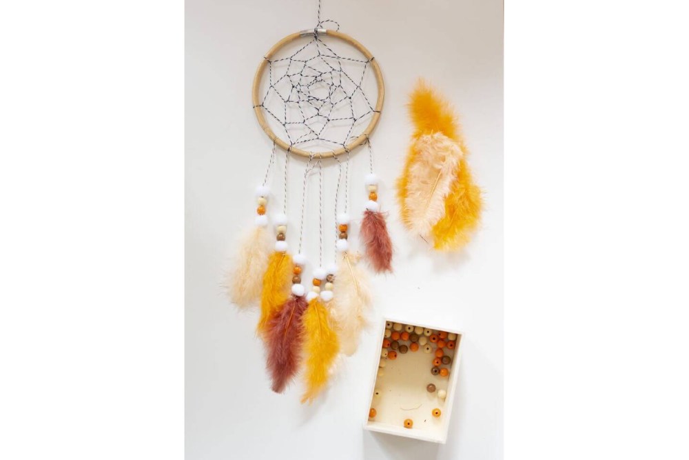 Bastelanleitung Do it yourself-Traumfänger für Kinder basteln. Schritt 2: Perlen, Pompons und Federn auffädeln und an den Holzring knoten.