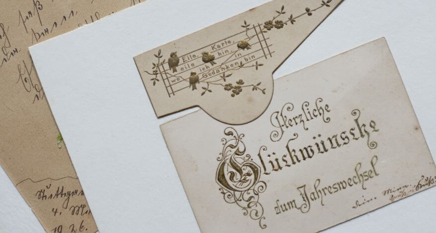 Ansicht einer historischen Postkarte mit Goldprägung. Auf der Grußkarte steht geschrieben "Herzlichen Glückwunsch zum Jahreswechsel".