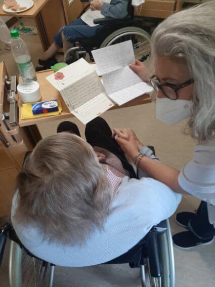 Der Bewohnerin eines Pflegeheims, die in einem Rollstuhl sitzt, wird ein Brief vorgelesen, den sie über die Initiative "Stift und Papier" erhalten hat.