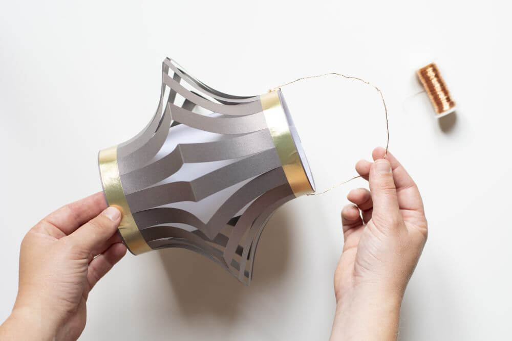 Laterne basteln aus Papier, Bastelanleitung Schritt 8: Stechen Sie für einen Henkel aus Draht zwei Seiten der Laterne mit einer Prickelnadel ein und fädeln Sie den Draht hindurch.