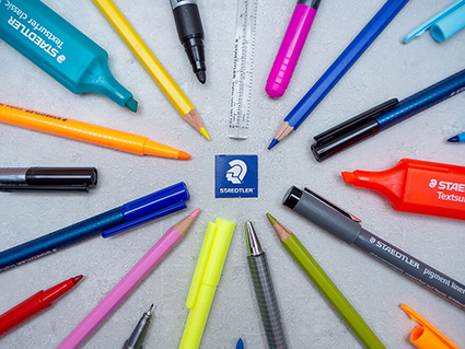 Verschiedene Stifte der Marke Staedtler auf einem Tisch zeigen auf ein Staedtler-Logo. Foto: Johanna Rundel