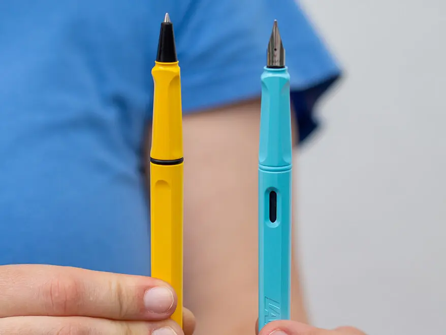Eine Person im blauen T-Shirt hält einen hellblauen Füller und einen gelben Tintenroller von Lamy in die Kamera.