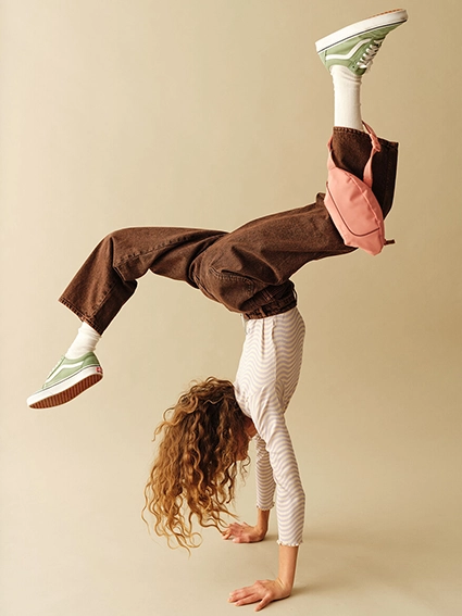 Ein Mädchen macht einen Handstand mit angewinkelten Beinen. Dabei hängt an ihrem vorderen Bein eine lachsfarbene Hip-Bag von satch.