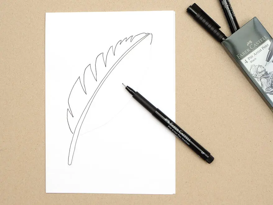 Auf ein Blatt wurde mit einem Pigmentliner von Faber-Castell eine Seite einer Vogelfeder gemalt. Ein Etui mit weiteren Finelinern liegt geöffnet daneben. Foto: Johanna Rundel