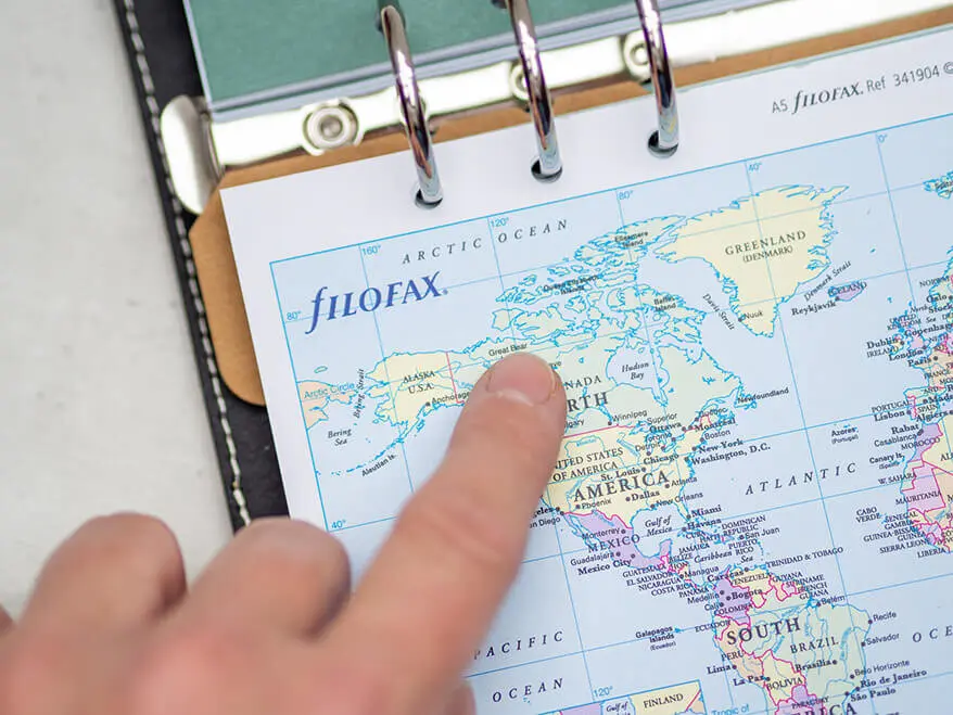Jemand zeigt mit dem Finger auf einer Weltkarte in einem Filofax-Organizer auf den Staat Kanada. Foto: Johanna Rundel