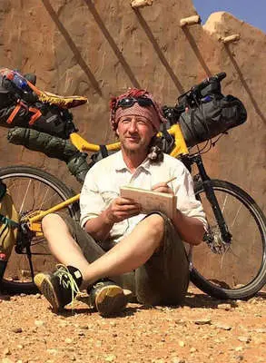 Künstler Jens Hübner sitzt zeichnend vor seinem Fahrrad in einer Wüste.