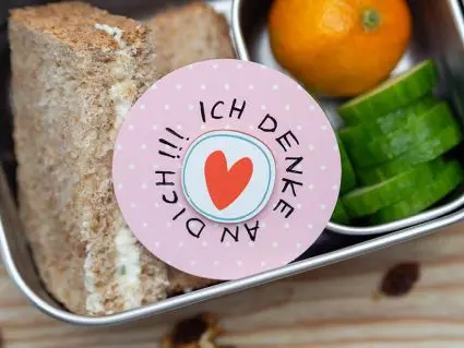 In einer gefüllten Edelstahlbrotdose von ergobag liegt ein runden Motivationskärtchen mit einem Herz und dem Spruch: „Ich denke an dich!“ Foto: Johanna Rundel