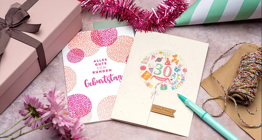 Auf einem rosa Untergrund liegen zwei Glückwunschkarten zum Geburtstag. Eine ist eine Letterpress-Karte von Rössler, die andere ist aus Aufklebern selbst gebastelt. Foto: Johanna Rundel 