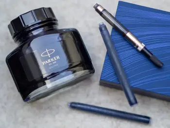 Auf einer hellen Filzmatte liegen verschiedene Tintensysteme für Füllfederhalter: Tintenfass und Konverter von Parker sowie eine Einweg-Tintenpatrone von Waterman. Foto: Johanna Rundel