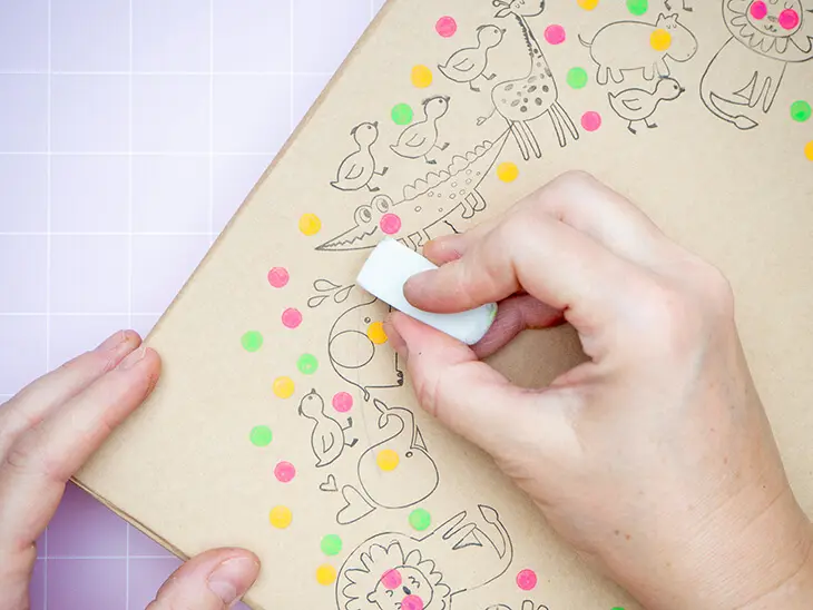 Jemand radiert einen Bleistiftkreis vom Deckel einer Pappschachtel von KNORR prandell, der mit Stempeln von HEYDA gestaltet ist. Foto: Johanna Rundel