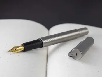 Ein schwarzer Füller von Otto Hutt liegt auf einem aufgeschlagenen, leeren Notizbuch.