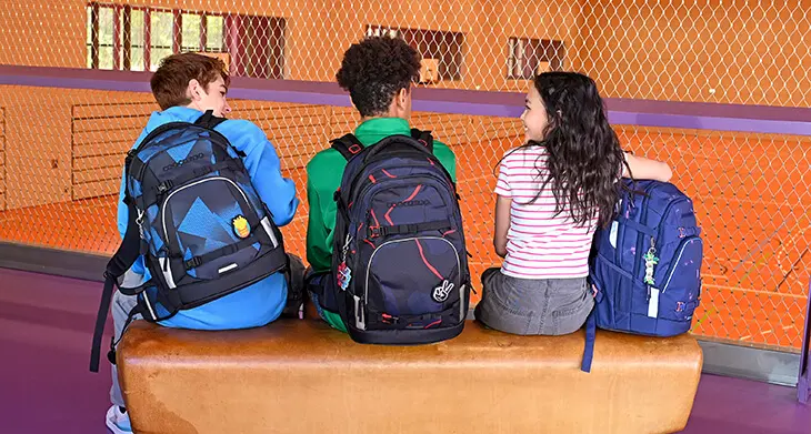 Drei Jugendliche sitzen mit ihren Schulrucksäcken von coocazoo in der Sporthalle auf einem Turnpferd.