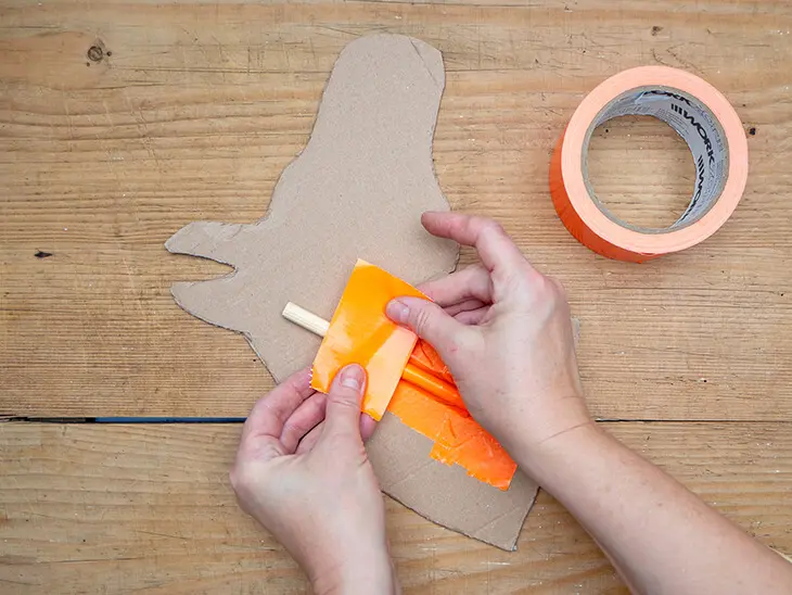 Jemand klebt mit orangefarbenem Panzertape ein Rundholz auf einen Pferdekopf aus Pappe. Foto: Johanna Rundel