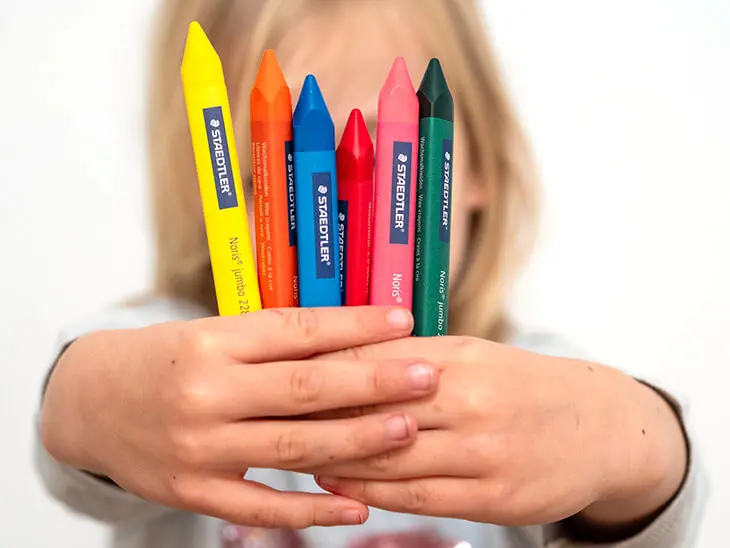Ein Kind hält bunte Wachsmalstifte von STAEDTLER in die Kamera. Foto: Johanna Rundel