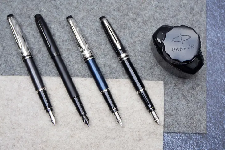 Vier Füllhalter und ein Tintenfass von Parker liegen auf einem Tisch.