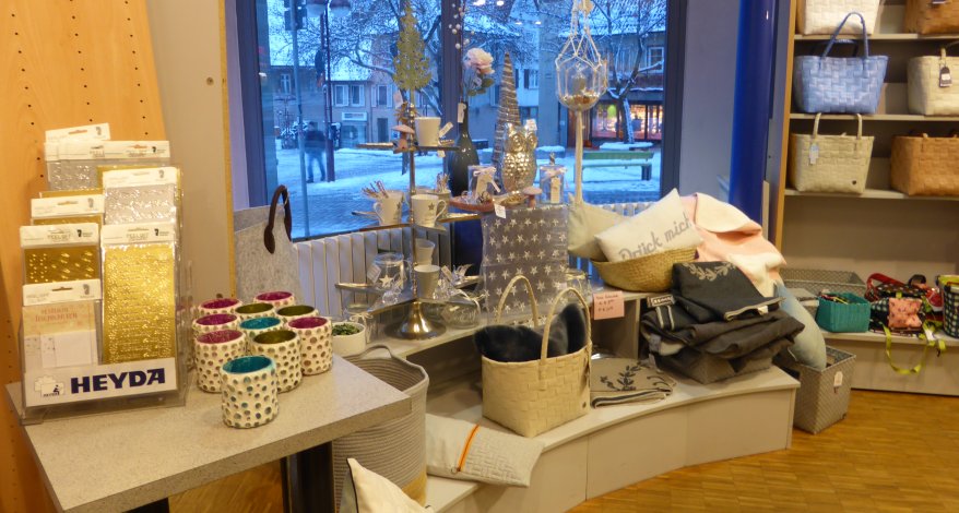 Diverse Decken, Tassen, Körbe und Teelichthalter stehen in einem Regal.