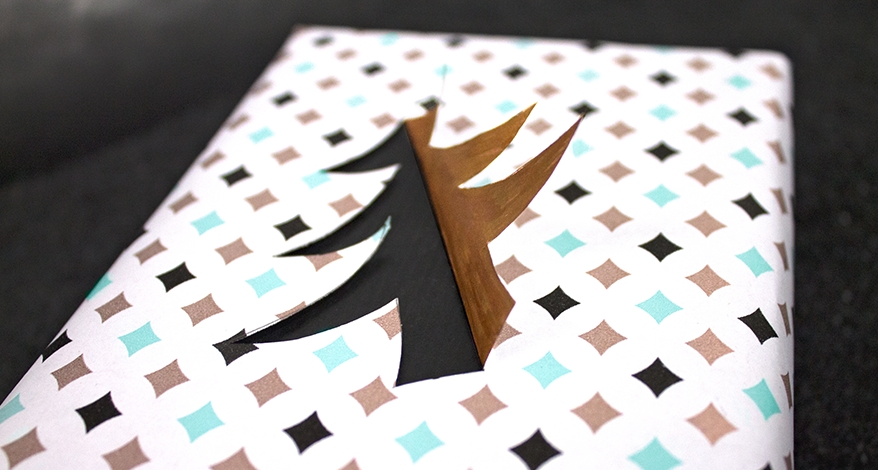 Nahaufnahme eines eingepackten Geschenks, welches mit einem schwarz-goldenem Tannenbaum verziert ist.