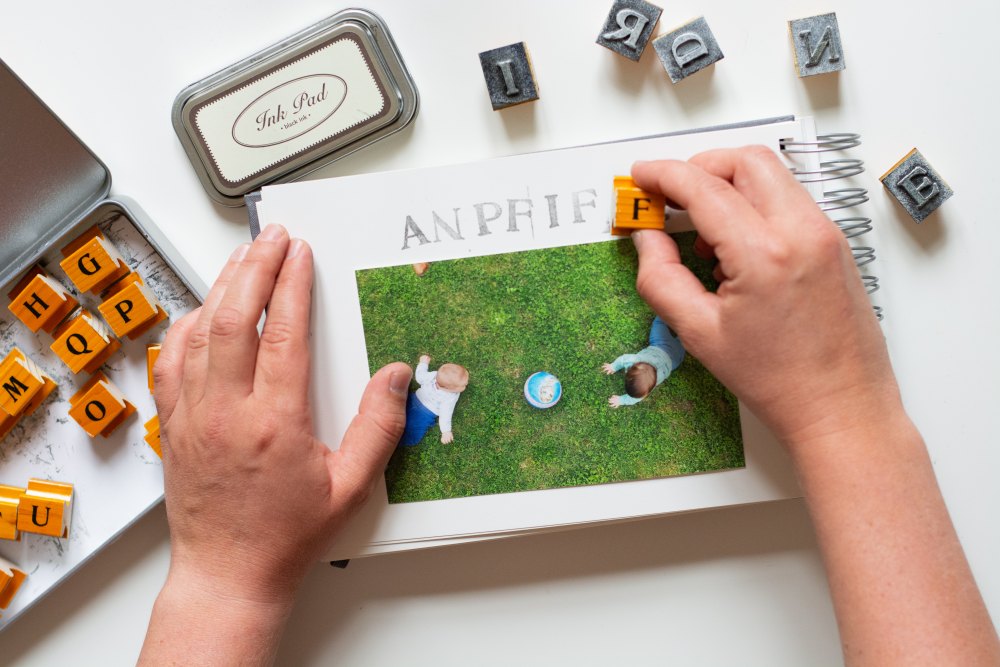 Mit Buchstabenstempeln wird das Wort "Anpfiff" in ein Fotoalbum gestempelt. Die einzelnen Buchstabenstempel liegen um das Fotoalbum herum. 