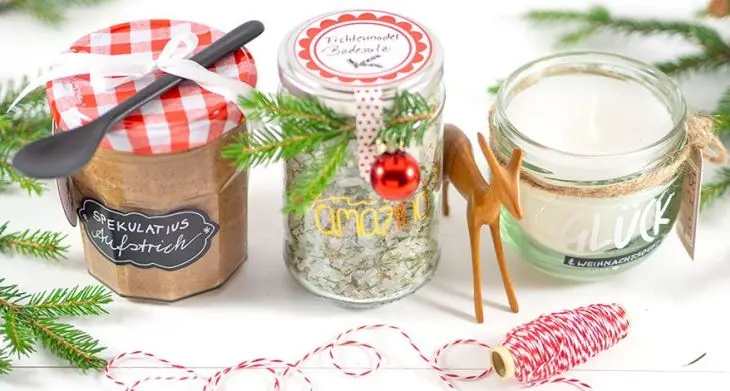 3 selbstgemachte Geschenke im Glas stehen auf einem Tisch, drumherum liegt Weihnachtsdeko