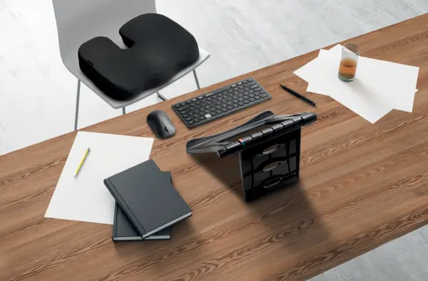 Das Bild zeigt einen modernen Arbeitsplatz mit einem ergonomischen Sitzkissen auf einem Stuhl, das für optimalen Sitzkomfort sorgt. Auf dem Tisch befinden sich eine Tastatur, eine Maus, ein Laptopständer, Notizbücher und Schreibutensilien, die eine produktive und komfortable Arbeitsumgebung unterstützen.