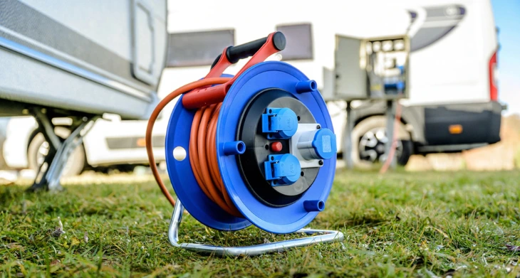 Verlängerungskabeltrommel vor Wohnmobil auf grünem Rasen.