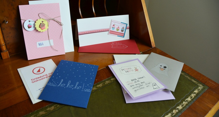 Auf einem Sekretär liegen viele verschiedene selbstgestaltete Einladungskarten.