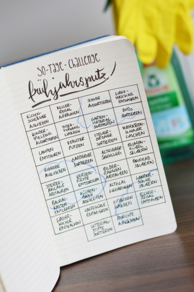 Notizbuch mit 30-Tage-Challenge „Frühjahrsputz“ und Reinigungsmittel und gelben Gummihandschuhen