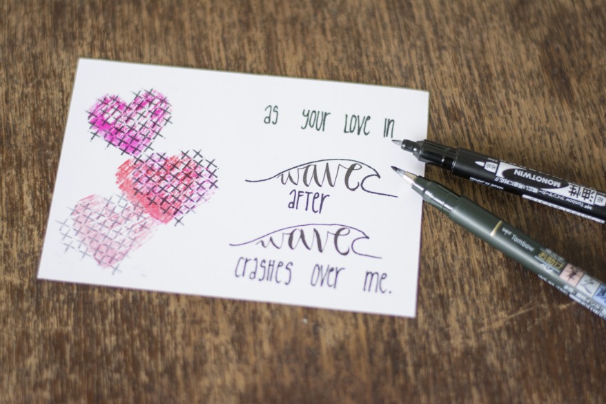Karte mit Lettering-Zitat und Herzstempeln, daneben zwei Brushpens.