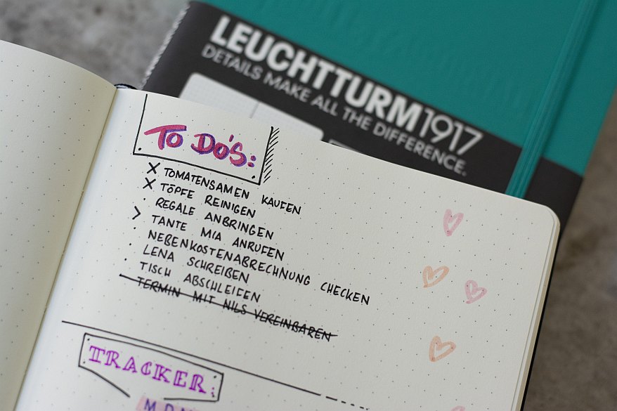 Nahaufnahme einer halben Seite eines Notizbuches. Dort ist eine To-Do Liste mit diversen Aufgaben eingetragen. Im Hintergrund ist ein Notizbuch der Marke Leuchtturm1917 zu sehen.