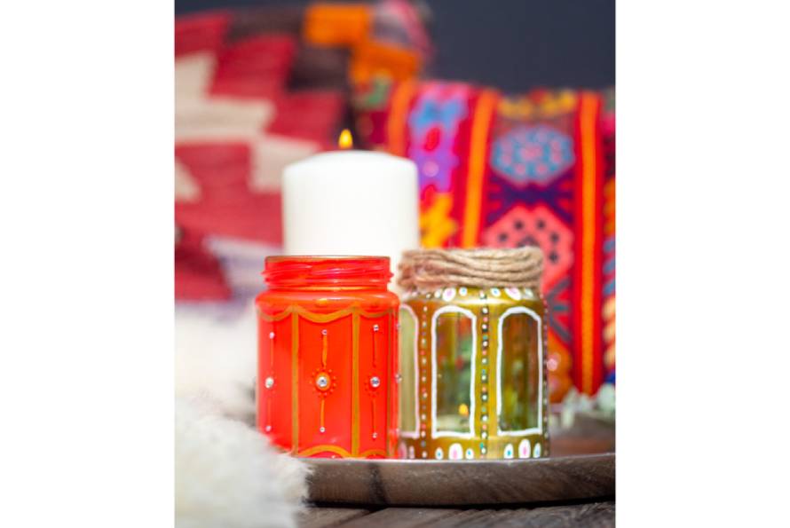 Mehrere bunte selbst gestaltete Windlichter auf einem Tablett, im Hintergrund bunte Kissen