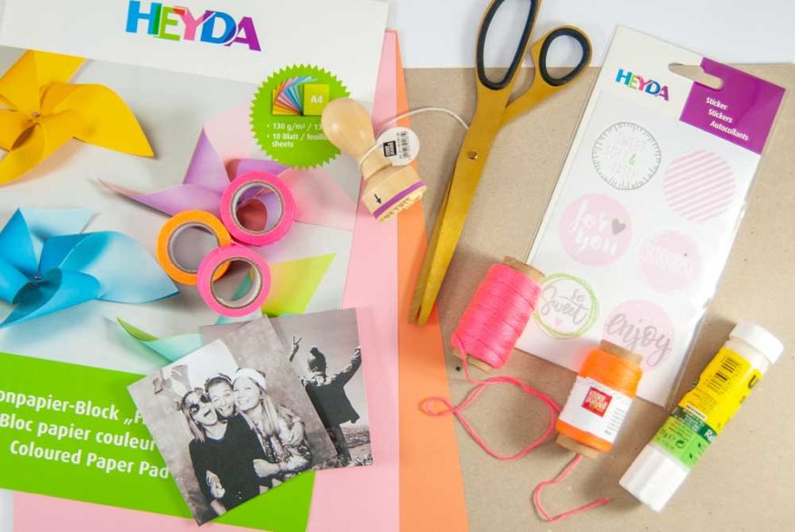 Auf einem Tisch liegen verschiedene Bastelmaterialien von Heyda und KNORR prandell, sowie eine Schere, ein Klebestift und Bastelkarton.