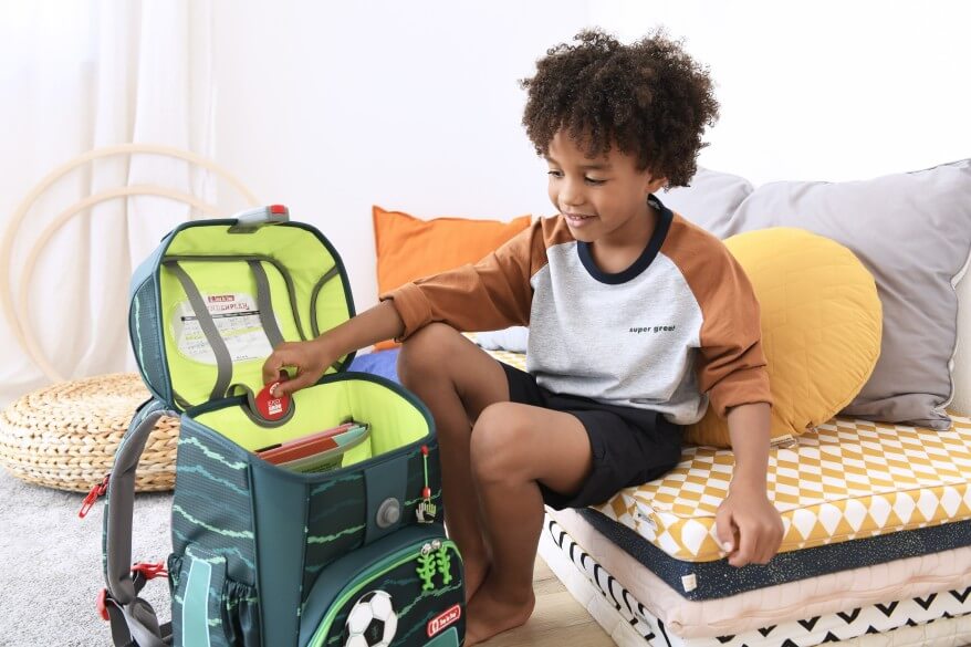 Ein Junge sitzt im Kinderzimmer und hat vor sich seinen aufgeklappten grünen Step by Step Schulranzen stehen.