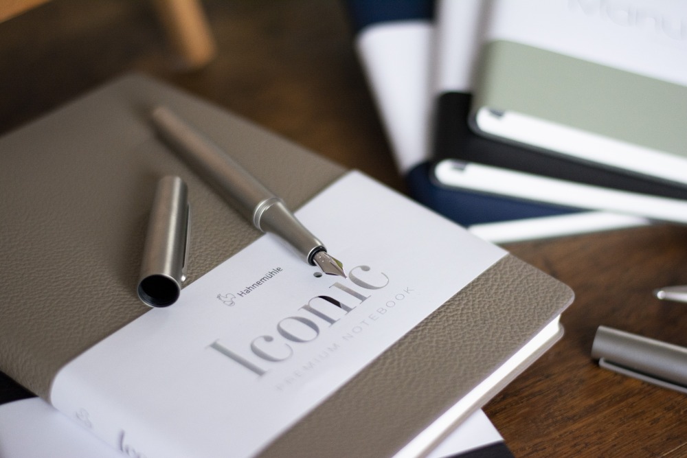 Füllhalter liegt mit offener Kappe auf Notizbuch Iconic von Hahnehmühle. Weitere Notizbücher Manuscript im Hintergrund.