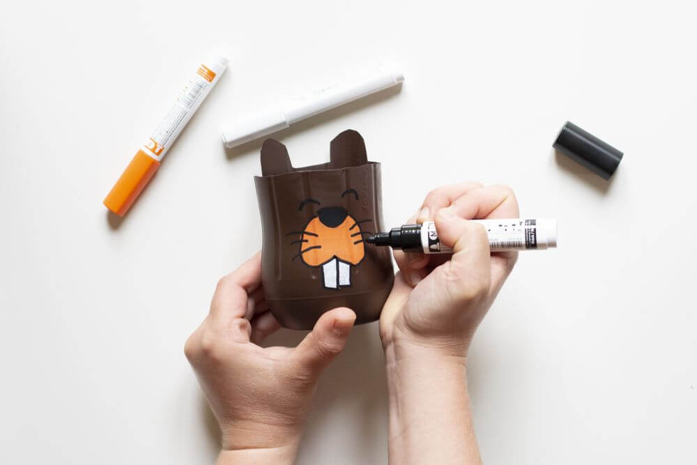 Ein Zahnputzbecher aus einer PET-Flasche wird mit Lackmarkern bemalt. Dieser sieht wie ein Biber aus.