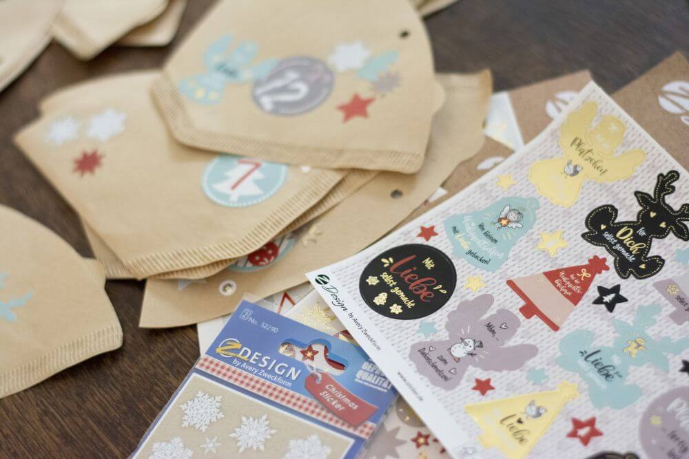 Close-up von beklebten Kaffeefiltern sowie Stickern mit Weihnachtsmoiven von Avery Zweckform.