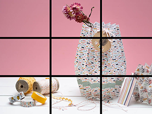 Ein Foto, auf dem eine Vase aus buntem Papier zu sehen ist. Links davon liegen verschiedene Bastelmaterialien von Knorr-Prandell und Heyda. Über dem Bild liegt ein Raster aus schwarzen Linien, dass das Bild in neun Teile teilt und die "Drittel-Regel" für Fotos beschreibt. Foto: Johanna Rundel