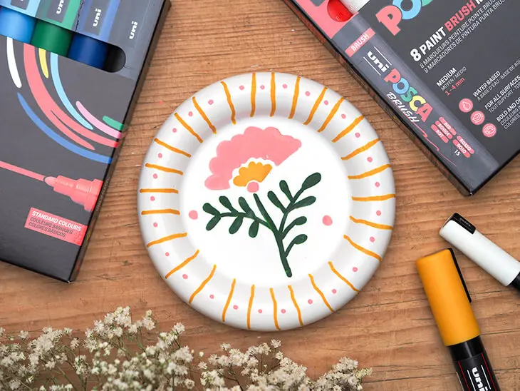 Ein bemalter Kerzenteller, daneben eine Packung Brush Marker von POSCA. Foto: Johanna Rundel