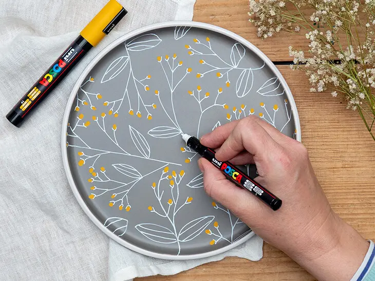 Jemand malt mit einem feinen POSCA Marker Blumen auf einen grauen Teller. Foto: Johanna Rundel
