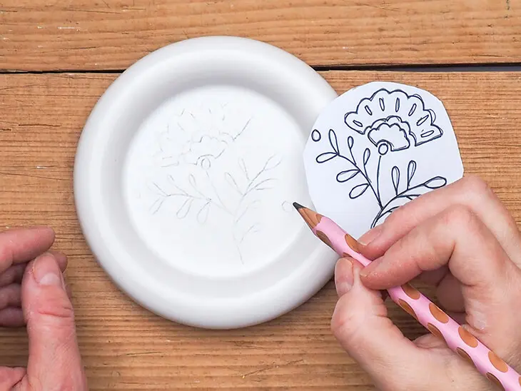 Jemand überträgt mit Bleistift ein Blumenmotiv auf einen Teller. Foto: Johanna Rundel