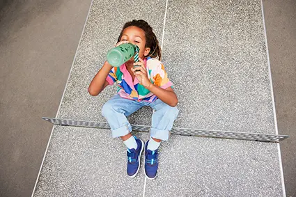 Zwei Grundschüler sitzen im Schneidersitz auf dem Gras und essen Obst und Gemüse aus ihren Brotboxen von ergobag.
