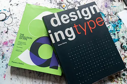 Auf einem mit Farbe beklecksten Untergrund liegen zwei Fachbücher zum Thema Typografie.