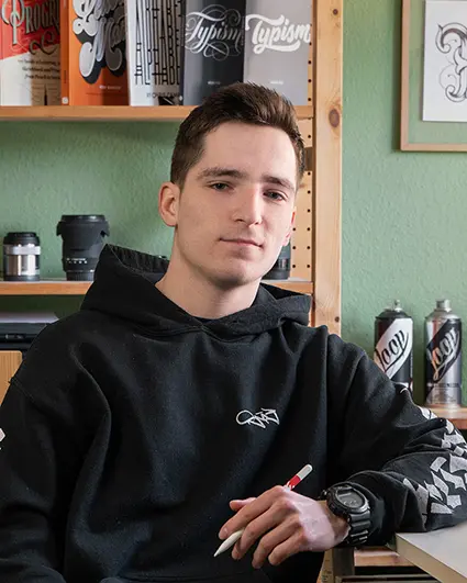 Der Berliner Artist Snooze One sitzt mit einem Stift in der Hand in seinem grünen Atelier.