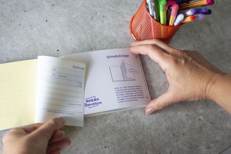 Jemand steckt eine Schreibeinlage zwischen die einzelnen Seiten eines Quittungsblocks. 