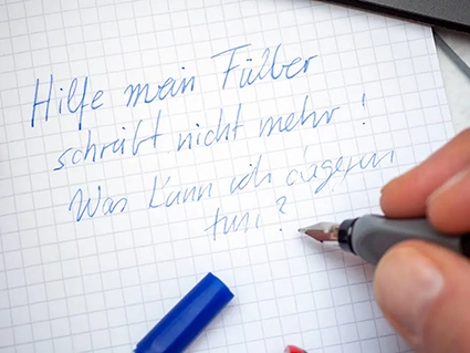 Jemand schreibt auf einem karierten herlitz-Notizheft mit einem Füller von Pelikan. Dabei geht beim letzten Satz die Tinte aus. Foto: Johanna Rundel