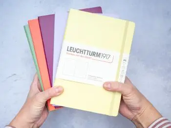 Jemand hält einen Stapel verschiedenfarbiger Notizbücher von LEUCHTTURM1917 ins Bild. Foto: Johanna Rundel