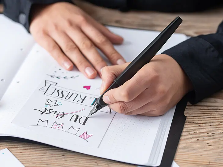 Jemand schreibt mit einem schwarzen Kalligrafie-Füller von Pelikan in ein Bullet Journal.